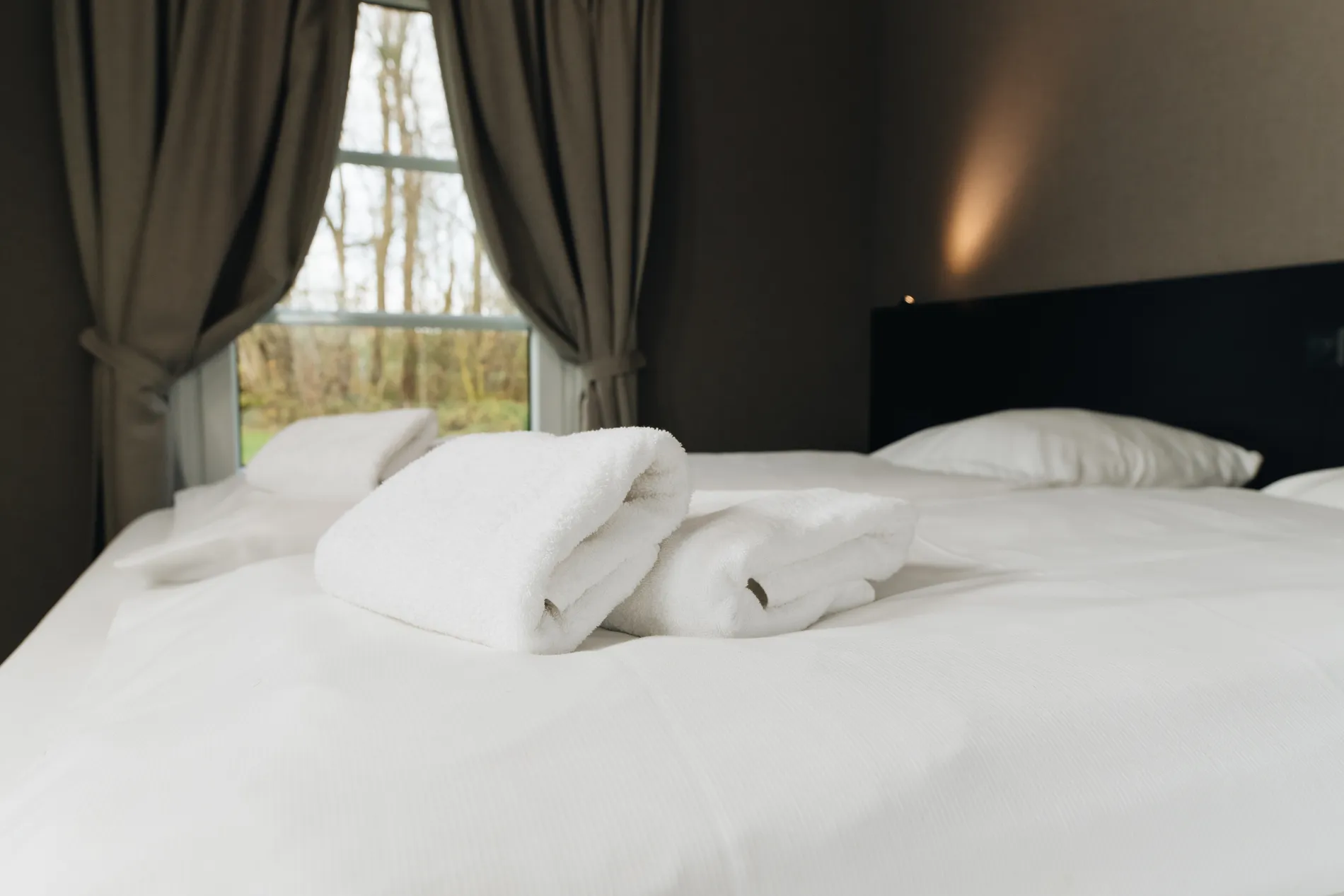 Detail van luxe, zachte witte handdoeken op een fris opgemaakt tweepersoonsbed in de hotelkamer.